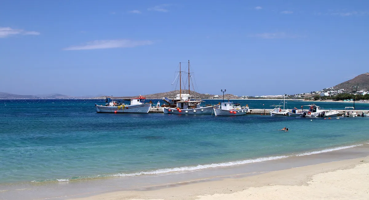 Fishing boats and tour boats moored at Agia Anna port in Naxos with turquoise water and swimmers