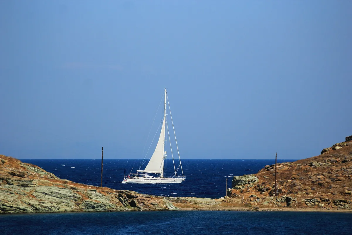 White sailing yacht passing between rocky headlands on deep blue Aegean water on a windy Cyclades day