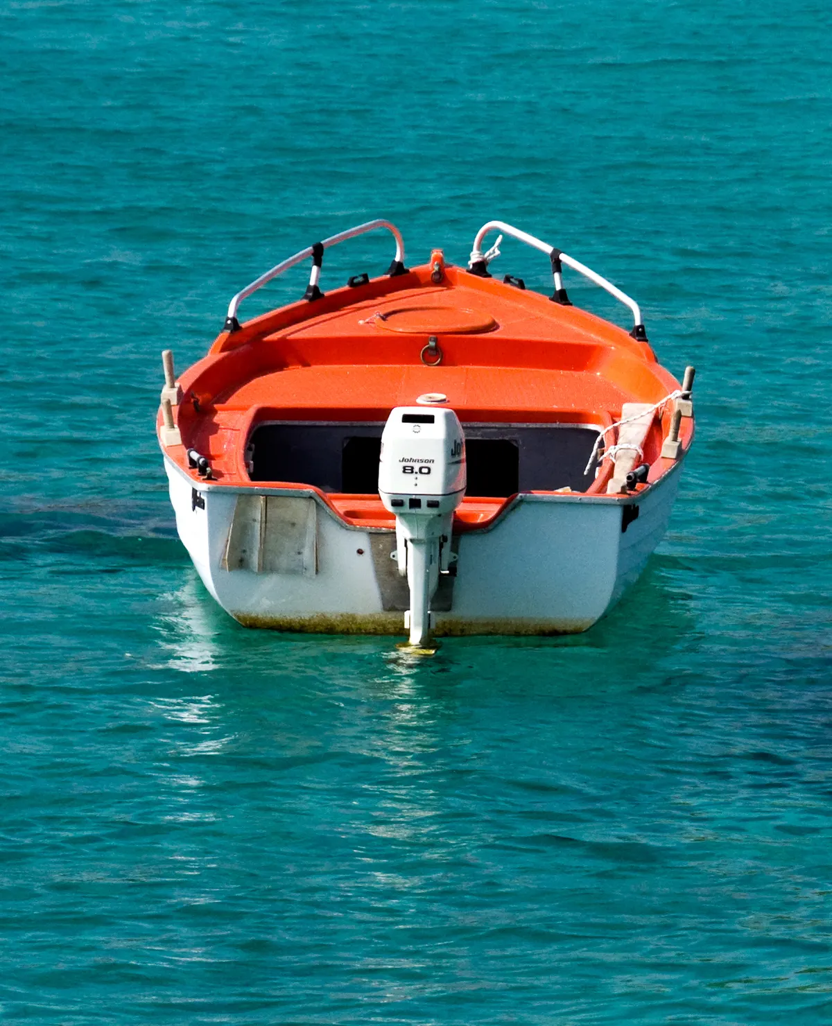 Small orange and white self-drive motorboat with outboard engine floating on turquoise Aegean water