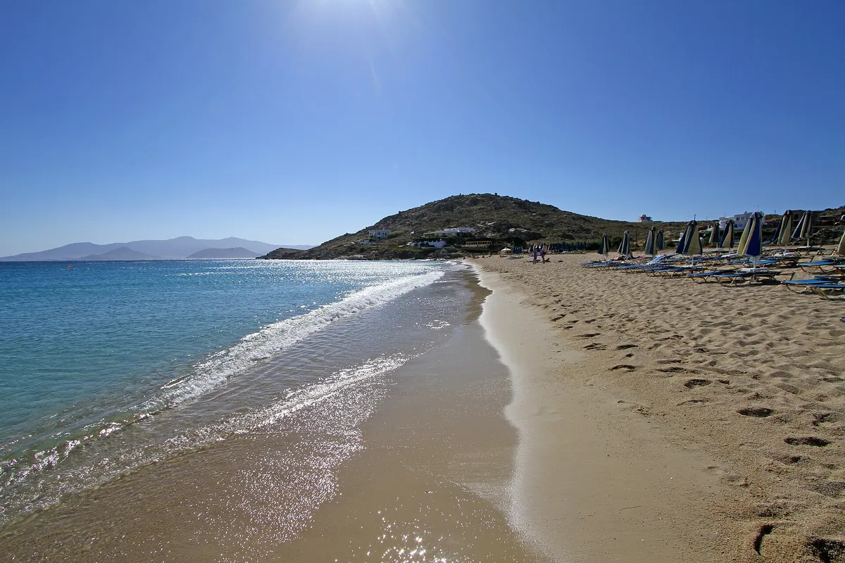 Sun glare over calm turquoise water and white sand at Agios Prokopios beach, Naxos, Greece