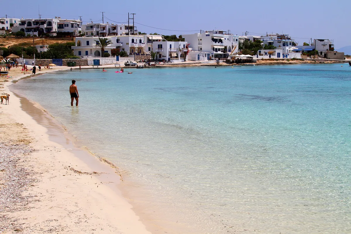 Whitewash village houses behind a sandy beach with turquoise water on Ano Koufonissi island, Greece