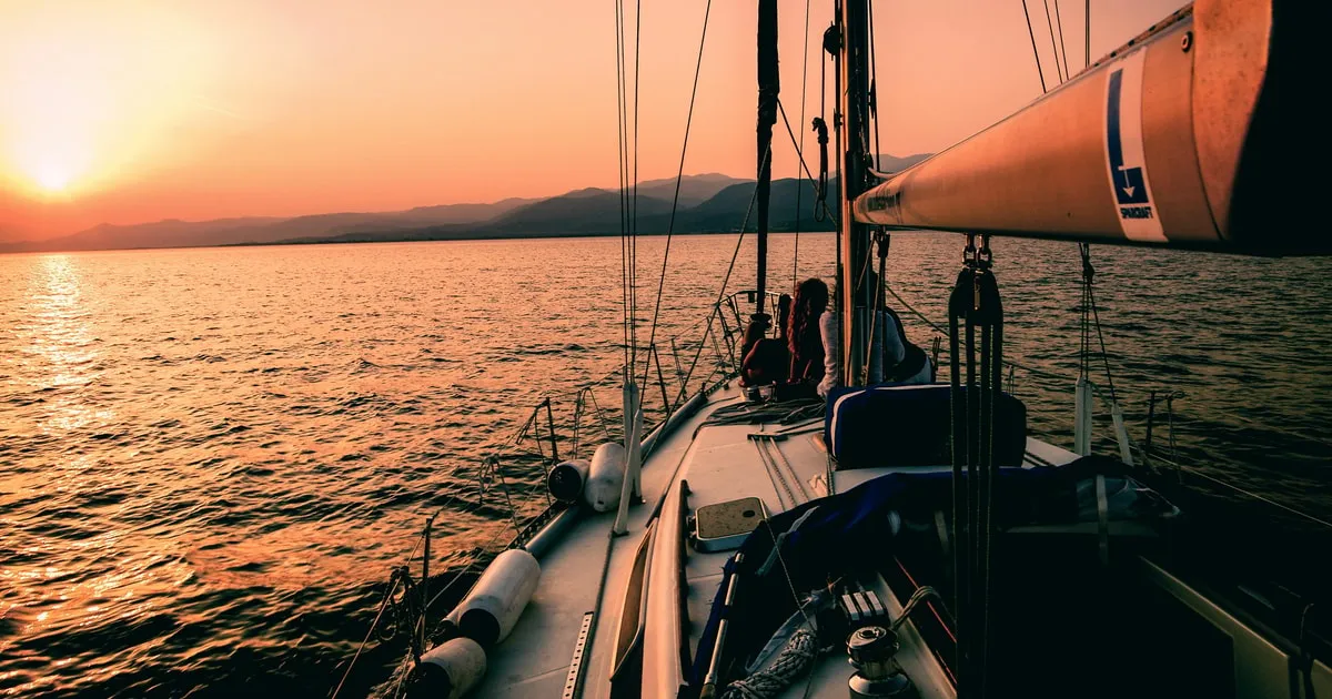 Sailboat silhouetted against a golden Aegean sunset on a Naxos sunset cruise with a swim stop