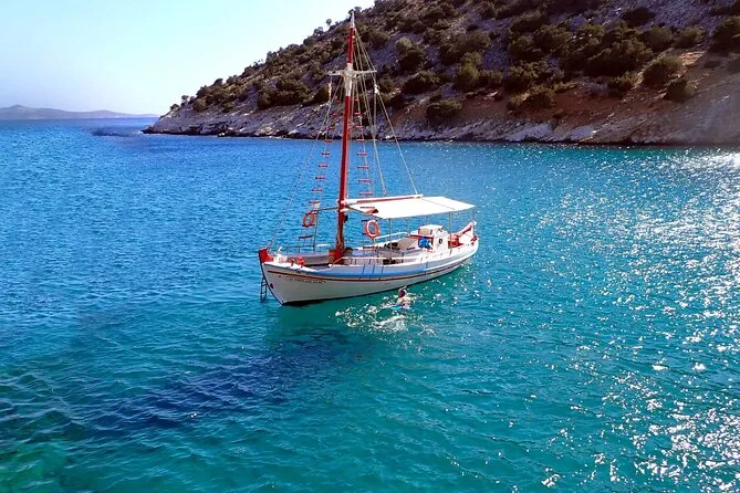 Traditional wooden boat at the mouth of a sea cave with swimmers on a Rina Cave boat trip from Panermos, Naxos