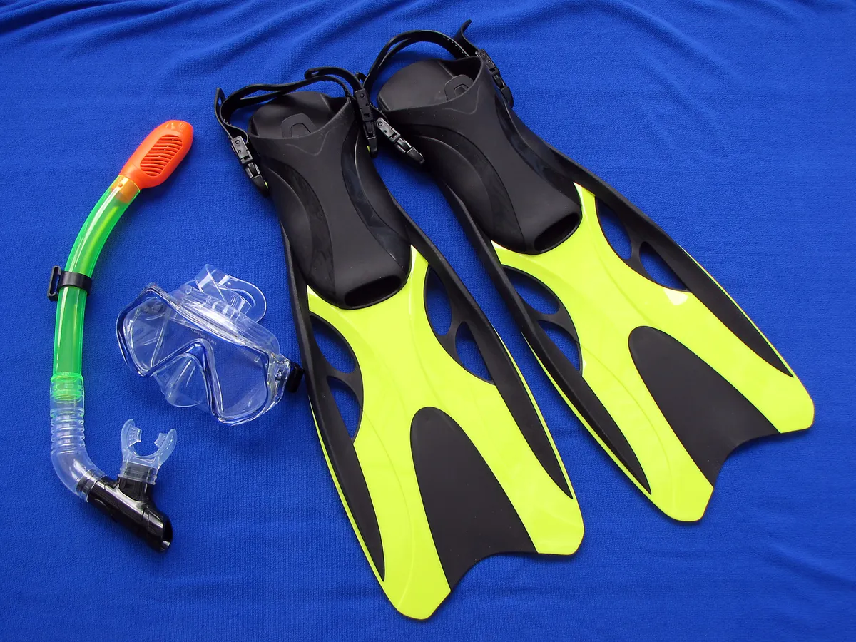 Snorkelling set of mask, snorkel and yellow-black fins laid out on a blue towel