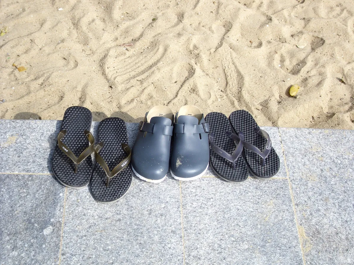 Two pairs of black flip flops and leather sandals left on golden beach sand