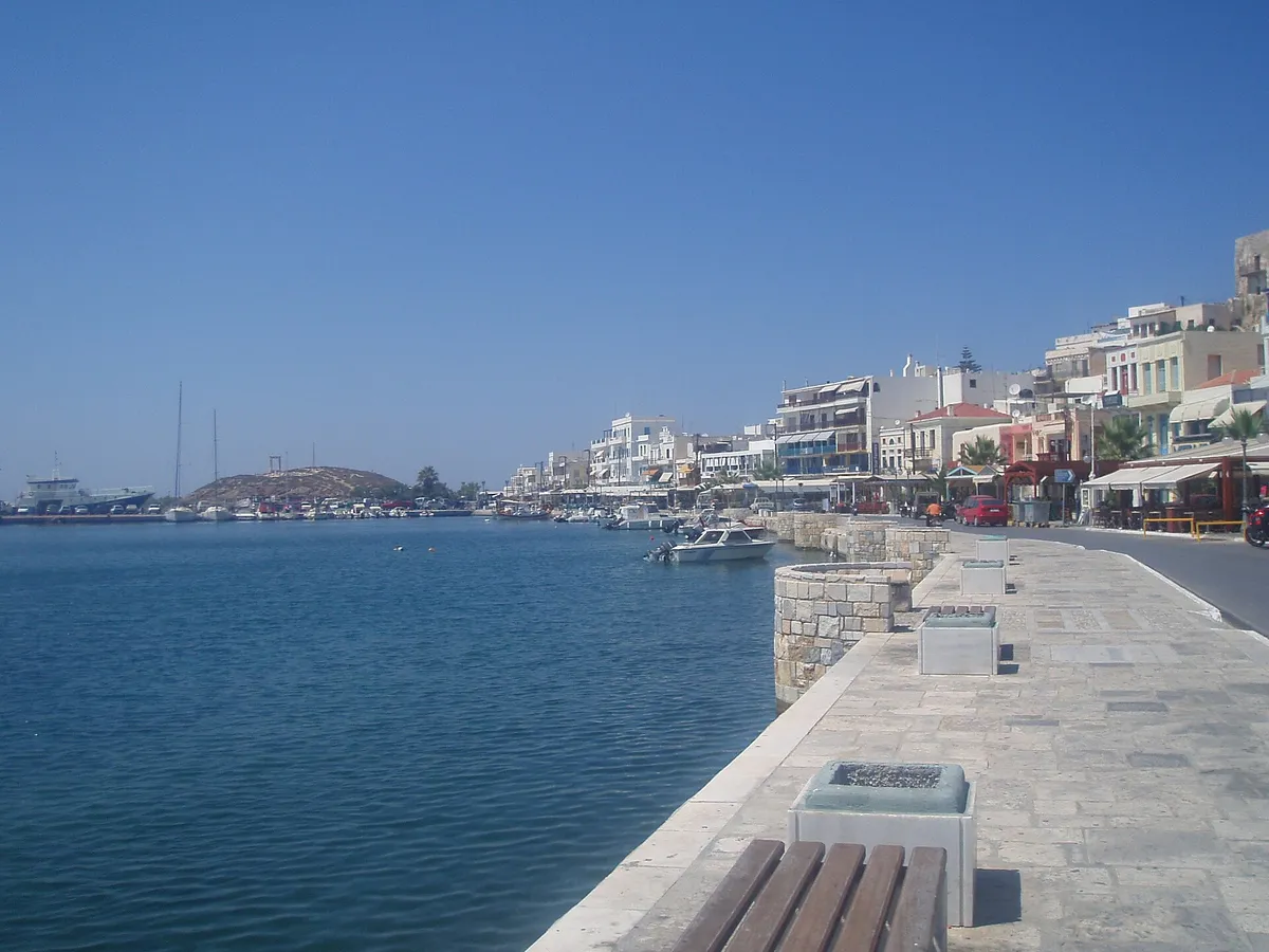 Cycladic island quay with whitewash buildings, moored boats and a stone waterfront promenade in Greece